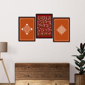 May include: Three framed art prints. Two prints feature orange backgrounds with white geometric designs and borders. The central print has a dark red background with a floral pattern of white flowers and green leaves. All are in black frames.