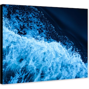 May include: A close-up of a wave crashing in the ocean. The water is a deep blue color and the foam is white. The image is taken from above the wave.