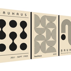 May include: Three beige canvas prints with black geometric designs. The first print features a pattern of black circles and ovals. The second print features a pattern of black semi-circles. The third print features a black curved line with a circle at the end. The text "BAUHAUS" is on the first and third prints. The text "Juli - Sept 1923" is on the first print. The text "bauhaus" is on the second print. The text "1919" is on the second and third prints. The text "Ausstellung 1919" is on the third print.