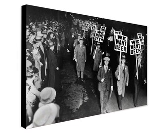 May include: Black and white photograph of a group of people marching down a street, holding signs that read "We Want Beer".