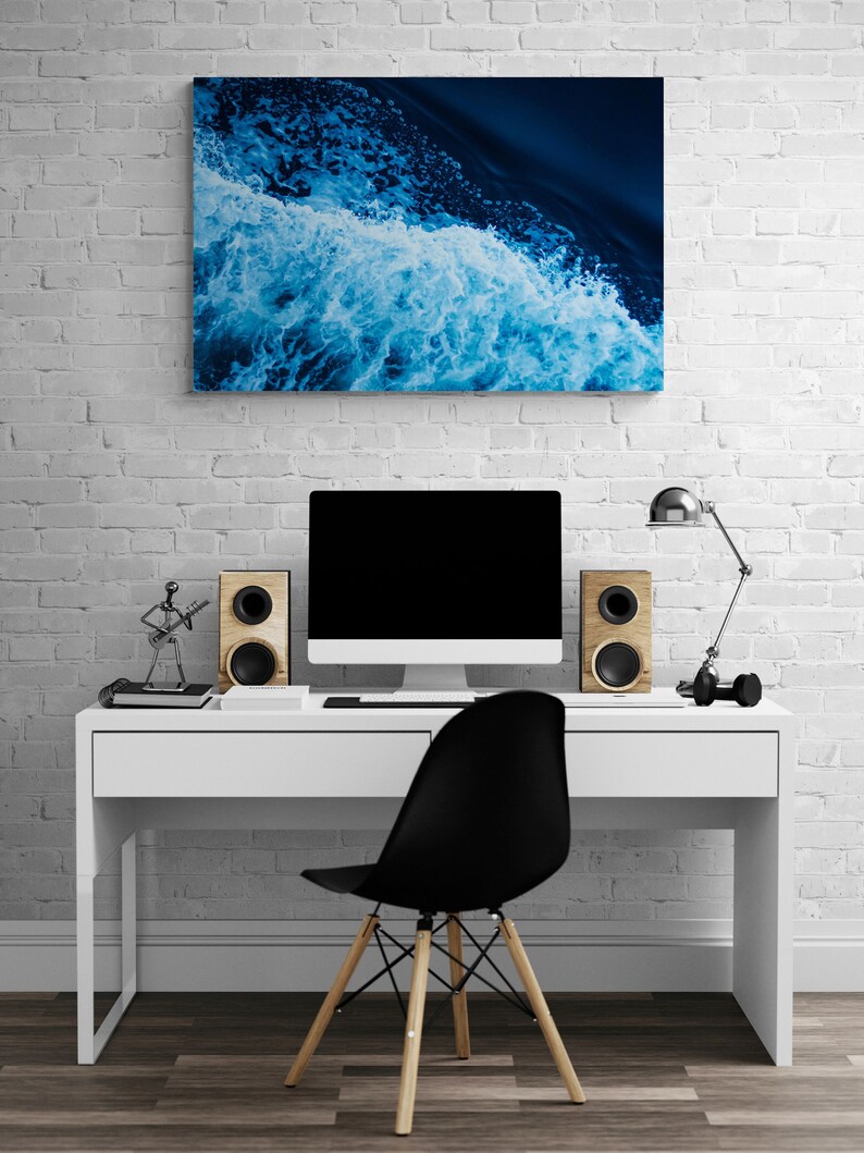 May include: A white desk with a black chair, a computer monitor, and two speakers. A blue and white abstract painting hangs on the wall behind the desk.