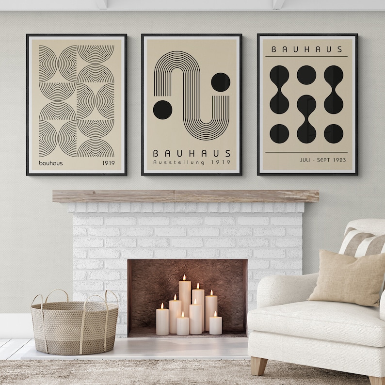 May include: Three framed prints with black and white geometric designs on a beige background. The prints feature the text "Bauhaus" and dates. The prints are hanging above a white brick fireplace.