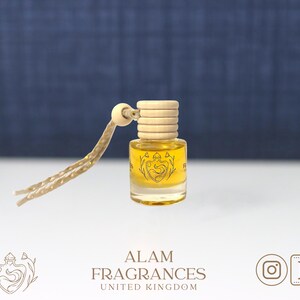 Könnte beinhalten: Eine kleine, durchsichtige Glasflasche mit einem Holzverschluss und einer daran befestigten Schnur. Die Flasche enthält eine gelbe Flüssigkeit und hat ein schwarz-weißes Design auf der Vorderseite. Das Design zeigt ein stilisiertes Herz mit einem floralen Motiv. Die Flasche ist mit "Alam Fragrances United Kingdom" beschriftet.