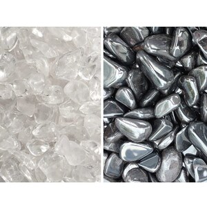 Könnte beinhalten: Eine geteilte Ansicht mit einer Sammlung kleiner, getrommelter klarer Quarzsteine auf der linken Seite und einer Sammlung kleiner, getrommelter metallisch dunkelgrauer Hämatitsteine auf der rechten Seite. Beide Steine haben glatte Oberflächen.