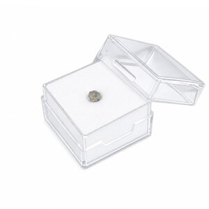 Könnte beinhalten: Ein kleines, raues, gräulich-braunes Mineralexemplar in einer quadratischen, transparenten Kunststoff-Präsentationsbox. Die Box verfügt über einen Klappdeckel und eine weiße Schaumstoffeinlage, die den strukturierten Stein mittig hält.