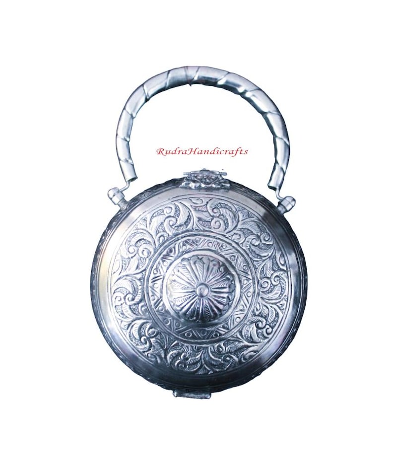 May include: A silver round box with an ornate design and a twisted handle. The box has a floral pattern and a central circular design. The text "Rudra Handicrafts" is visible on the box.