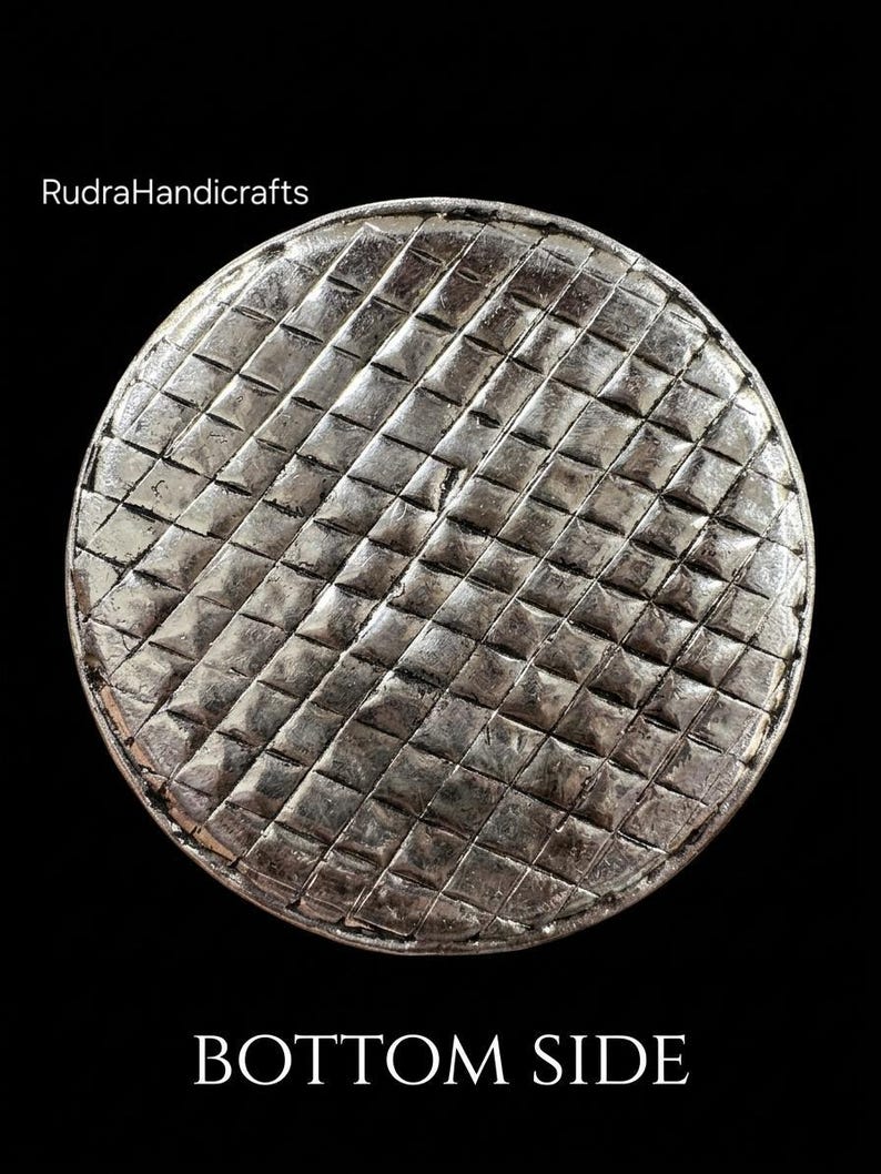 May include: A circular silver-toned object with a textured grid pattern of small raised squares across its surface. The text RudraHandicrafts is visible in the upper left corner, and the text BOTTOM SIDE is printed at the bottom of the image.