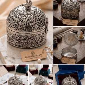 May include: A round silver-toned metal box with intricate filigree floral patterns and a bird-shaped finial on the lid. The box features a hinged opening and comes with a tan paper tag labeled RudraHandicrafts Handmade with Heritage.