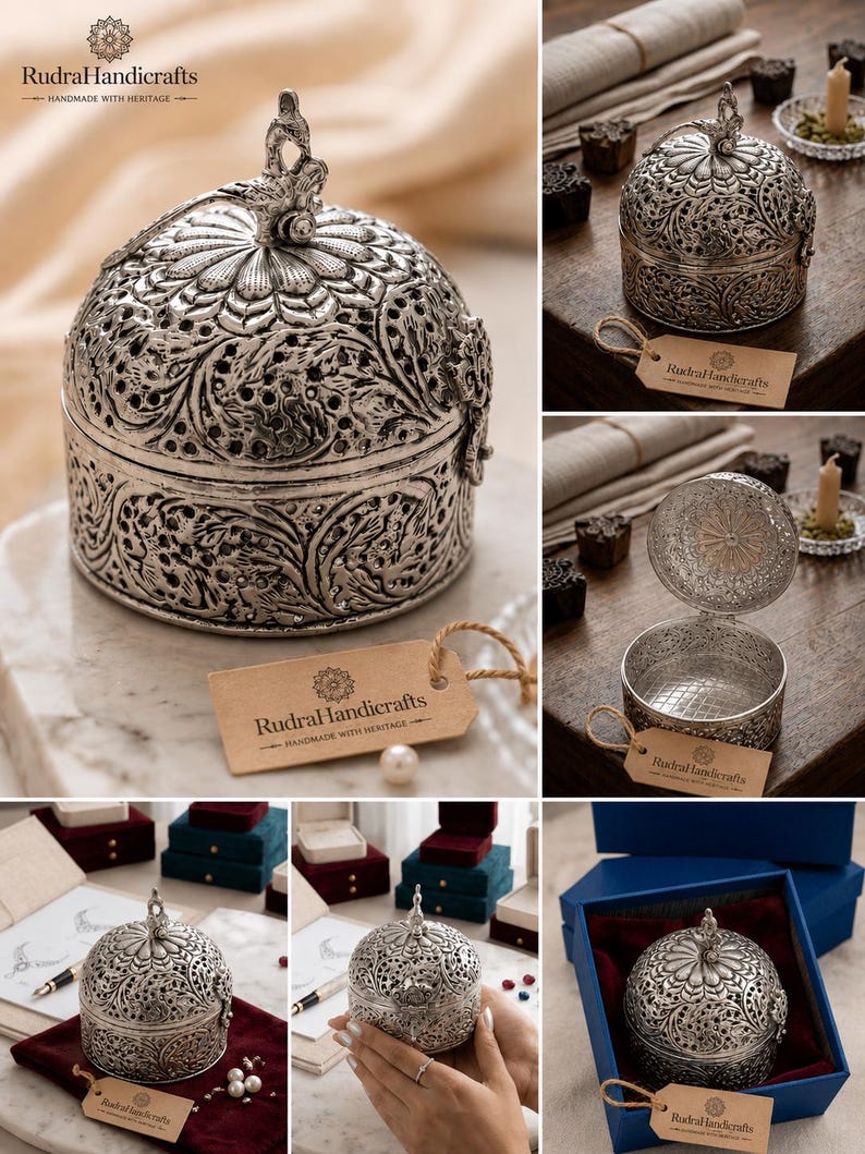 May include: A round silver-toned metal box with intricate filigree floral patterns and a bird-shaped finial on the lid. The box features a hinged opening and comes with a tan paper tag labeled RudraHandicrafts Handmade with Heritage.