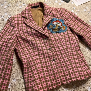 May include: A pink and brown patterned blazer with a mushroom-shaped embroidered patch on the right side of the chest.