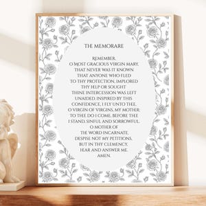 Pode incluir: Impressão emoldurada com o texto da oração do Memorare, rodeada por uma borda floral de rosas. O texto está centrado em um fundo branco, com o título no topo. A moldura é de cor de madeira clara.