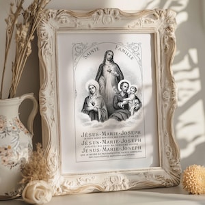 Puede incluir: Una impresión enmarcada con una imagen religiosa de la Sagrada Familia. La impresión en blanco y negro está dentro de un marco blanco ornamentado. El texto en la parte inferior dice "JÉSUS-MARIE-JOSEPH". El marco está junto a un jarrón decorativo.