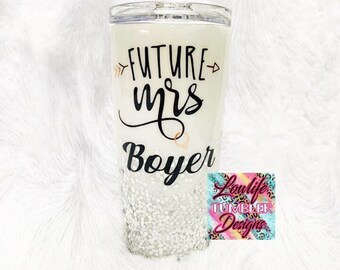May include: White tumbler with a black design that says "Future Mrs. Boyer" with glitter on the bottom. The tumbler has a clear lid and a pink and blue sticker that says "Loulife Tumbler Designs".