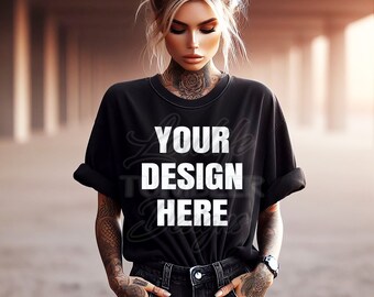 Op de afbeelding: Een zwart T-shirt met de tekst "YOUR DESIGN HERE" in wit op de voorkant. Het shirt wordt gedragen door een persoon met tatoeages.