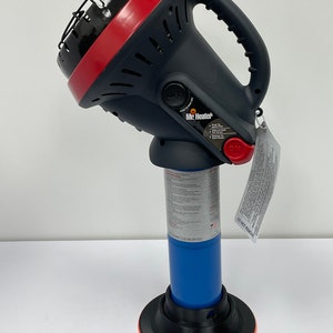May include: A black and red Mr. Heater portable propane heater. The heater has a black handle, a red top, and a blue propane tank base. The heater has an "ON" and "OFF" switch and a safety label. The base is black with an orange ring.