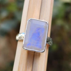 K&ouml;nnte beinhalten: Ein silberner Ring mit einem rechteckigen, schillernden Mondstein. Der Stein hat eine blaue und wei&szlig;e Farbe.