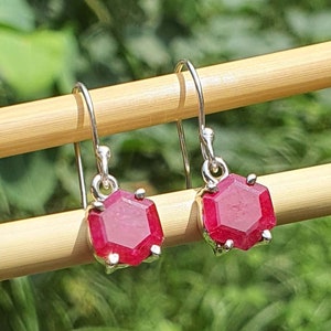 Könnte beinhalten: Ein Paar silberne Ohrhänger mit roten Edelstein-Akzenten. Die Edelsteine sind facettiert und haben eine sechseckige Form.