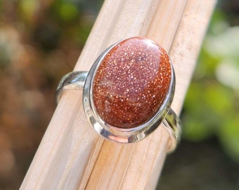 May include: A silver ring with a brown oval-shaped gemstone. The gemstone has a speckled texture.