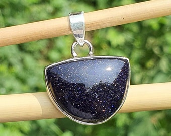May include: A silver pendant featuring a dark blue, half-moon shaped gemstone with a sparkly, textured surface.