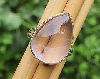 Pode incluir: Um anel em forma de lágrima com uma gema transparente rosa claro engastada em uma banda de prata.