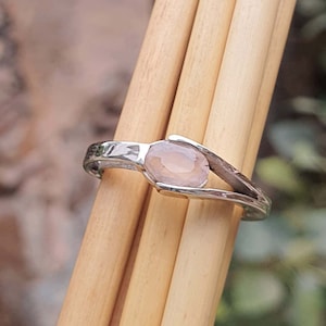 Könnte beinhalten: Ein silberner Ring mit einem zarten Design, das einen blassrosa ovalen Edelstein zeigt.