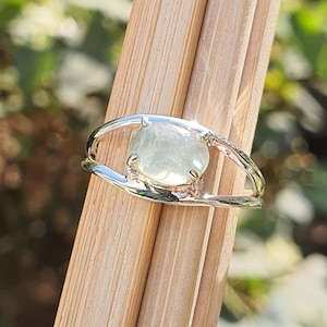 Peut inclure: Une bague en argent avec un design ouvert délicat mettant en valeur une pierre ovale vert clair.