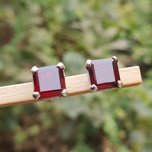 Könnte beinhalten: Ein Paar silberne Ohrstecker mit quadratischen roten Edelsteinen.