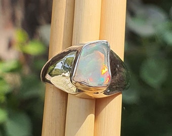 May include: A silver ring with a large, iridescent opal gemstone set in a bezel setting.