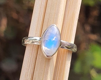 May include: A silver ring featuring a pearlescent moonstone gemstone. The stone displays a blue iridescent sheen.
