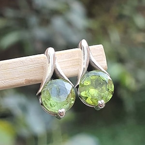 May include: A pair of silver earrings with green gemstone drops. The earrings have a delicate, curved design.