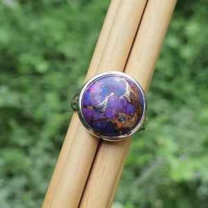 May include: A silver ring with a round purple and copper gemstone set in a bezel setting.