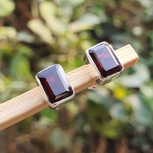 May include: A pair of silver earrings with red rectangular gemstones. The earrings are on a wooden surface.