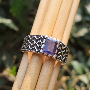 Könnte beinhalten: Ein silberner Ring mit geometrischem Muster und einem quadratischen violetten Edelstein.