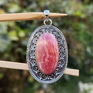 Pode incluir: Um pingente de prata com uma gema oval rosa e branca engastada em um design filigranado.