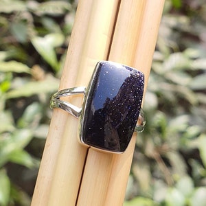 May include: A silver ring with a dark blue, rectangular gemstone. The gemstone has a sparkly, speckled texture.