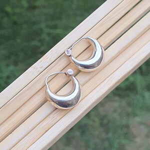 May include: A pair of silver hoop earrings with a rounded, half-moon shape. The earrings are marked with "925" on the back.