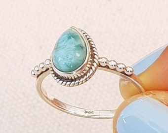 May include: A silver ring with a teardrop-shaped blue gemstone set in a beaded band. The ring is marked "925" on the inside.