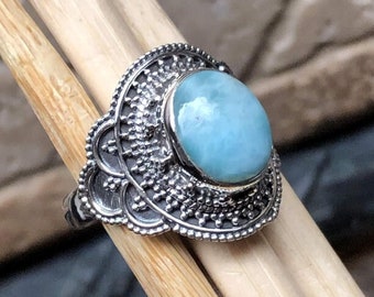 May include: A silver ring featuring a blue and green gemstone set within an ornate filigree design.