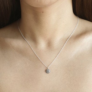 K&ouml;nnte beinhalten: Eine silberfarbene Halskette mit einem kleinen, runden Anh&auml;nger, der ein Sonnen- und Mondgesicht zeigt. Der Anh&auml;nger h&auml;ngt an einer zarten, d&uuml;nnen silberfarbenen Kette, die auf dem Schl&uuml;sselbein aufliegt. Das Metall hat eine polierte Oberfl&auml;che.