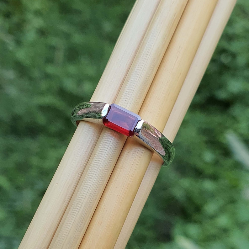 May include: A silver ring with a rectangular red gemstone set in the centre.