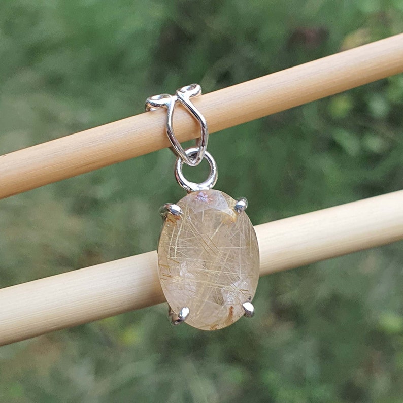 May include: A silver pendant featuring a clear quartz stone with gold inclusions. The stone is oval shaped and set in a silver bezel.