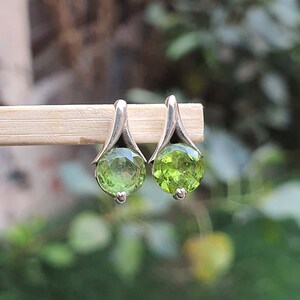 May include: A pair of silver earrings with green gemstone accents. The earrings have a delicate, curved design and feature round, faceted gemstones.