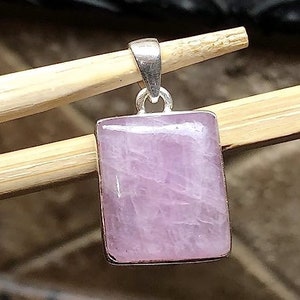 Peut inclure: Un pendentif en argent avec une pierre pr&eacute;cieuse rectangulaire rose clair. Le pendentif est sur une surface en bois.