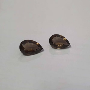 May include: Two pear-shaped brown gemstones, also known as smoky quartz, are displayed on a white surface.