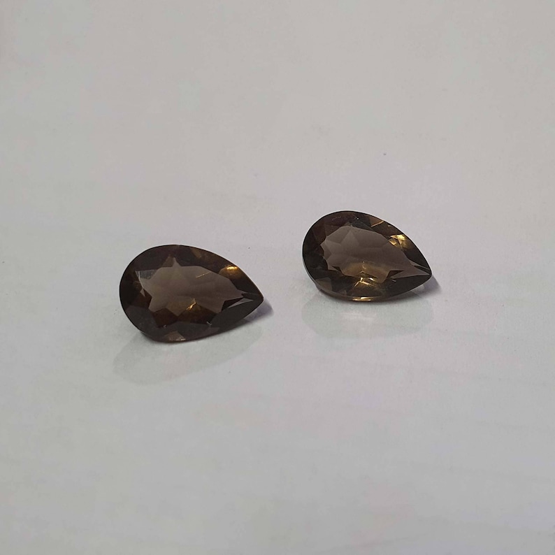 May include: Two pear-shaped brown gemstones, also known as smoky quartz, are displayed on a white surface.
