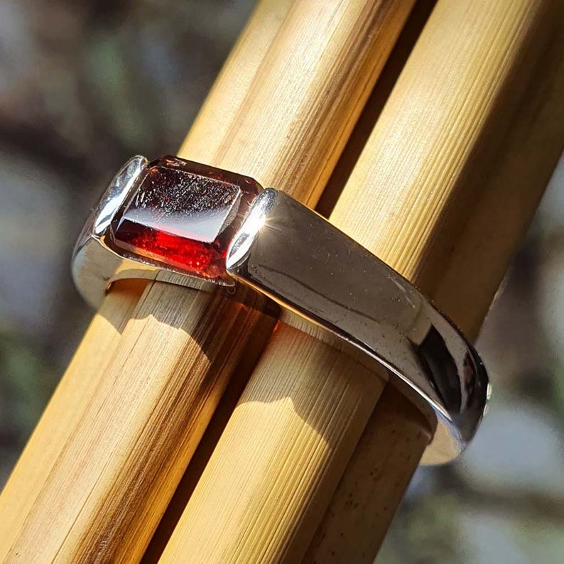 May include: A silver ring with a rectangular red gemstone set in the centre.
