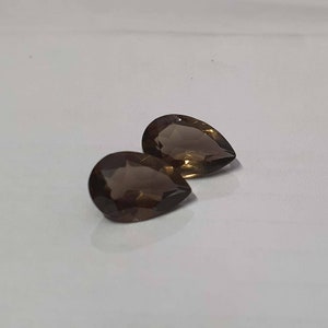 May include: Two pear-shaped smoky quartz gemstones. The gemstones are a dark brown color and have a faceted cut.