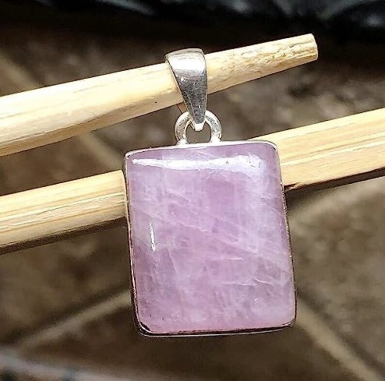 Peut inclure: Un pendentif en argent avec une pierre pr&eacute;cieuse rose de forme carr&eacute;e. Le pendentif est sur une surface en bois.