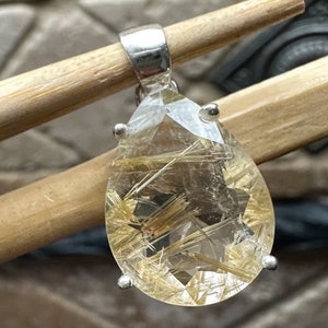 May include: A silver pendant featuring a teardrop-shaped clear quartz crystal with gold inclusions. The crystal is set in a silver bezel and has a silver bail.