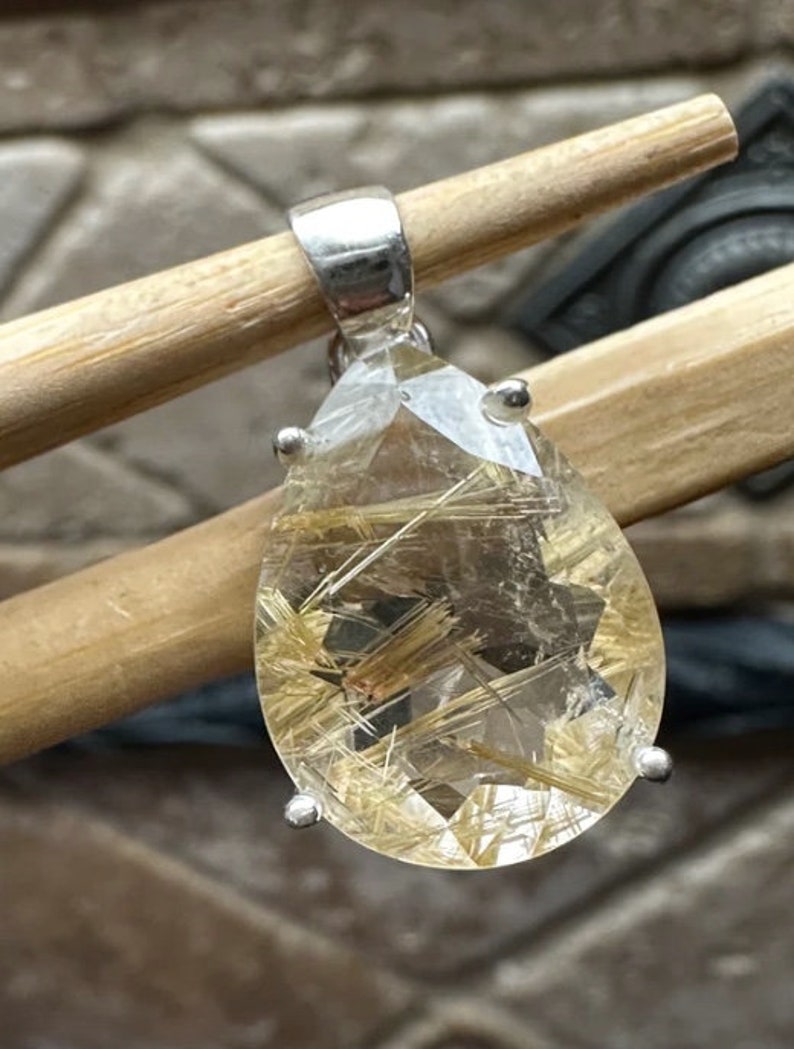 May include: A silver pendant featuring a teardrop-shaped clear quartz crystal with gold inclusions. The crystal is set in a silver bezel and has a silver bail.